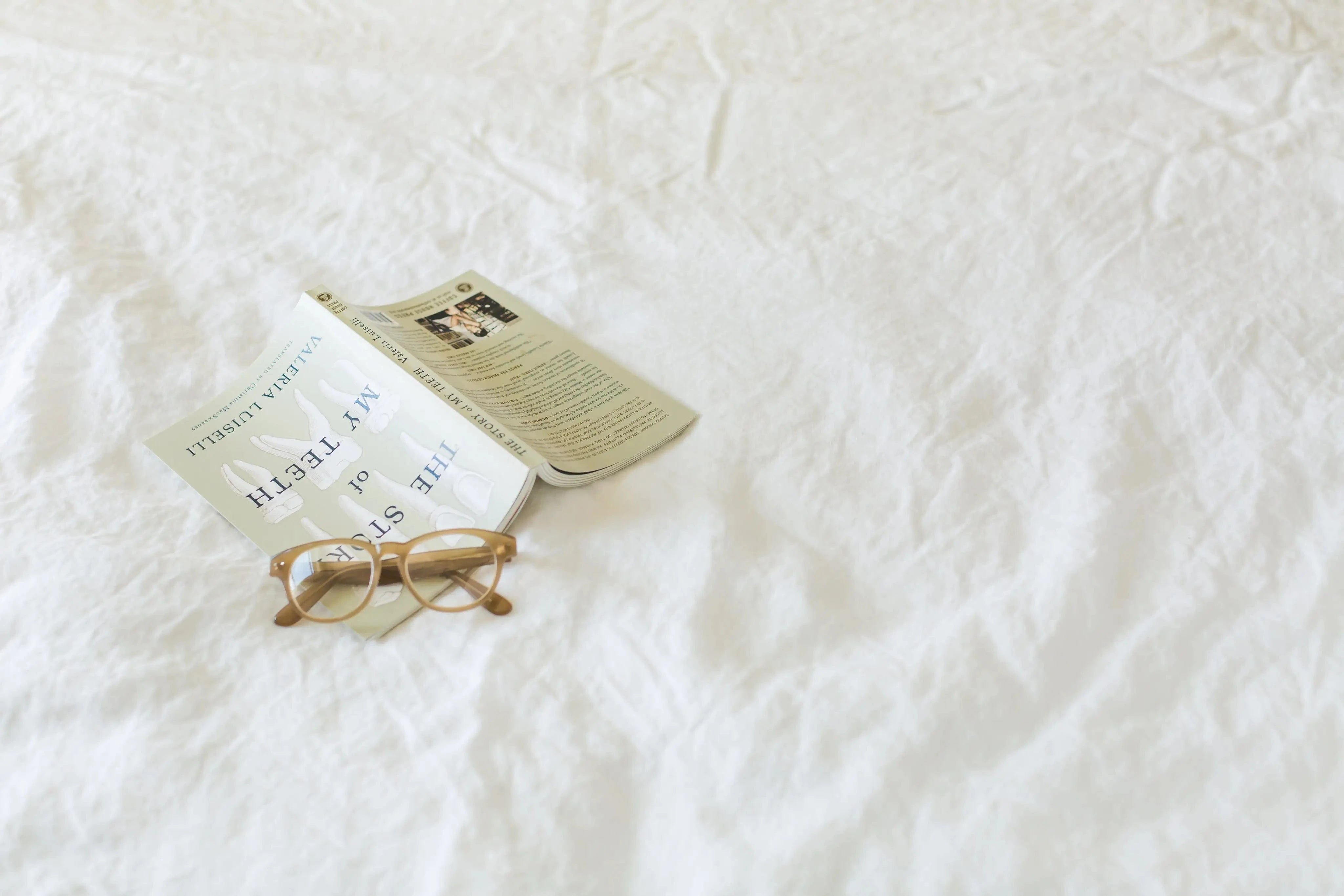 A book and glasses resting on a linen fabric surface.