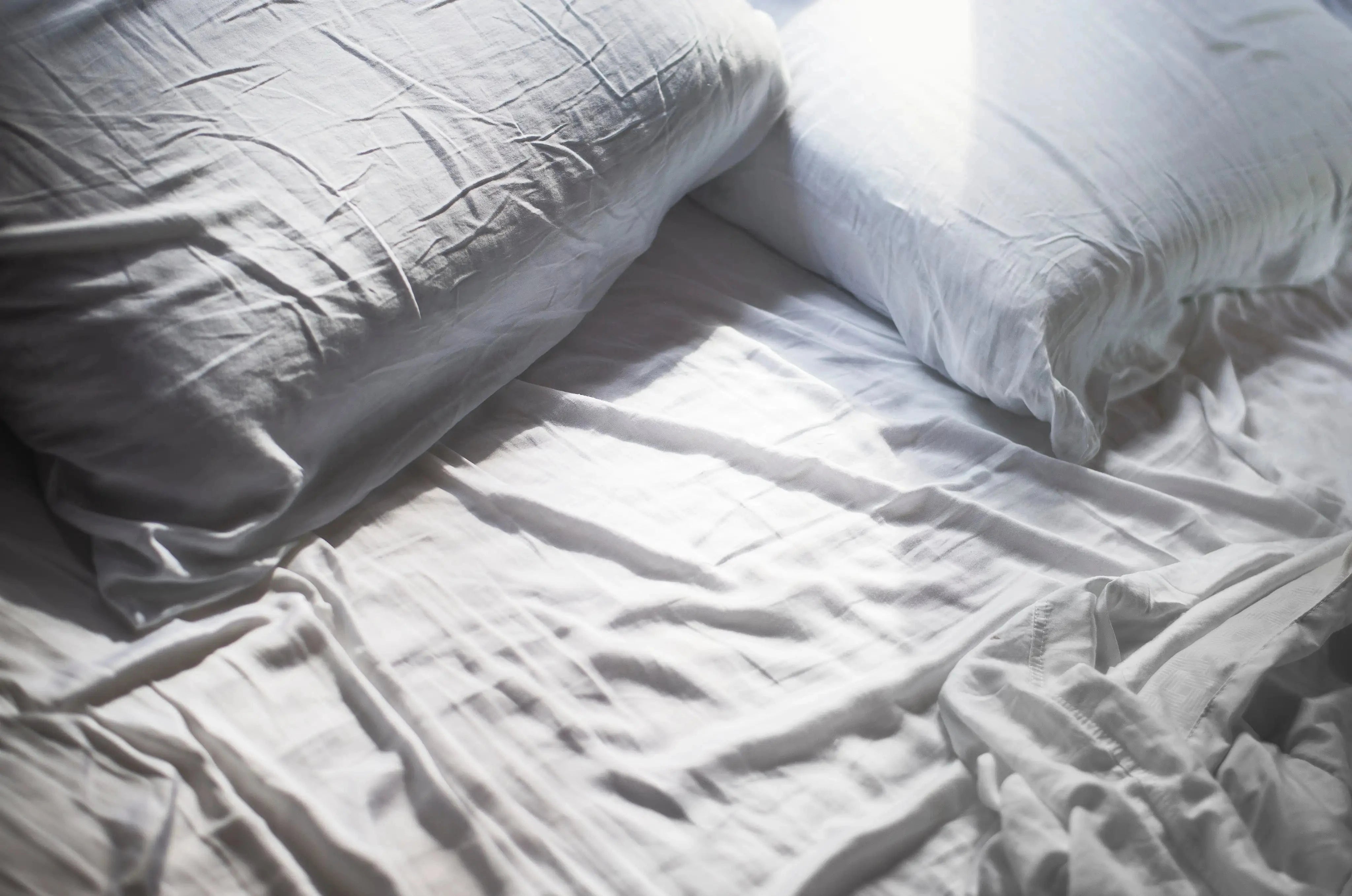 An unmade bed featuring white pillows and sheets.